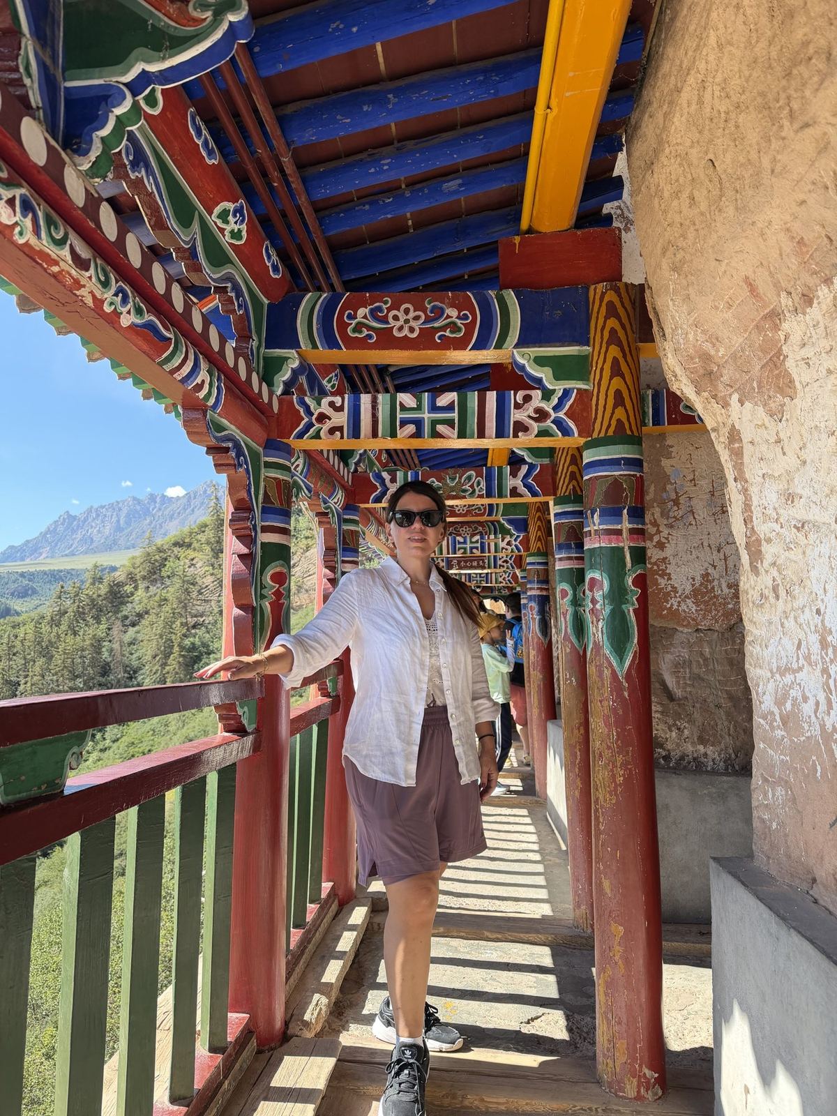 Linda on a painted wooden gallery along the Mati Temple cliff, Qilian Mountains behind