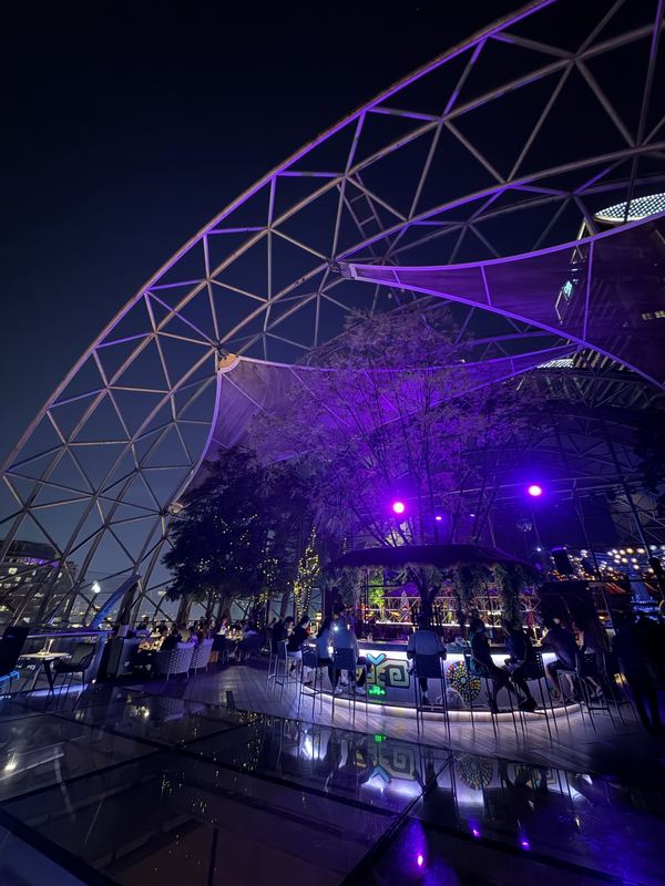 The glass dome of SHUA sky bar inside The Crystal, lit purple at night, with a tree and a round bar