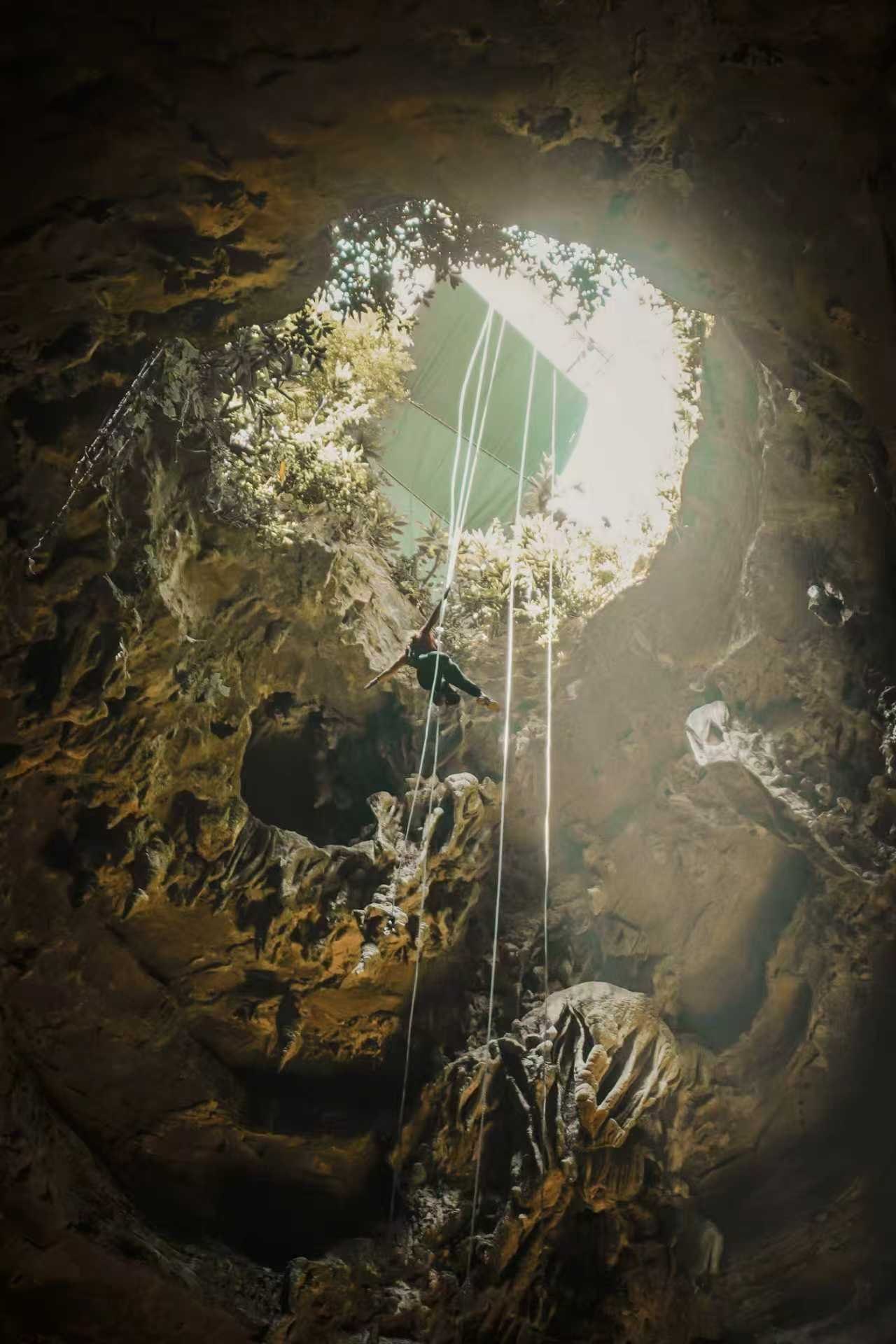 An abseiler on ropes hanging from the round opening of Tianyan Cave