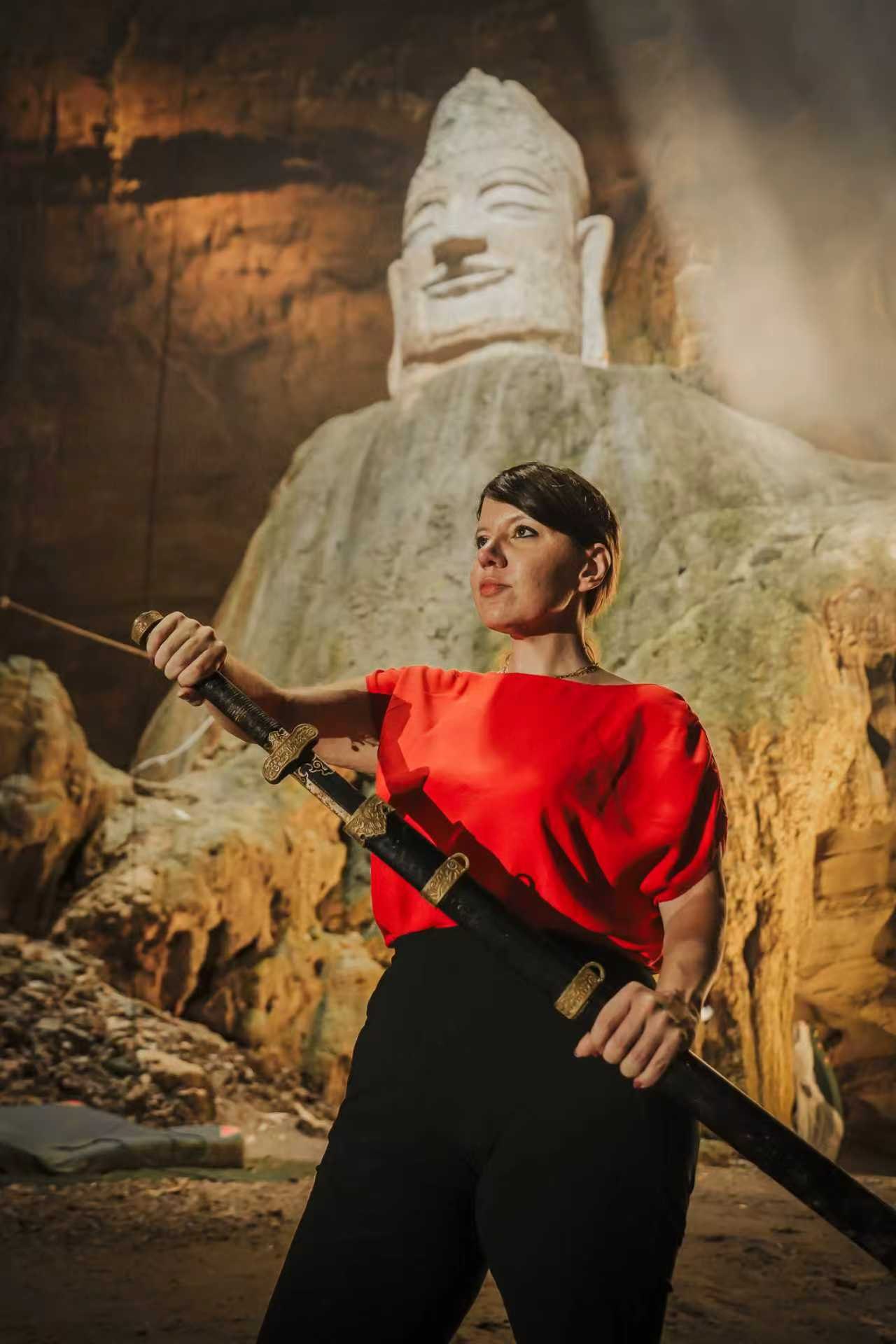 Linda posing with a sword in front of the stone Buddha in Tianyan Cave
