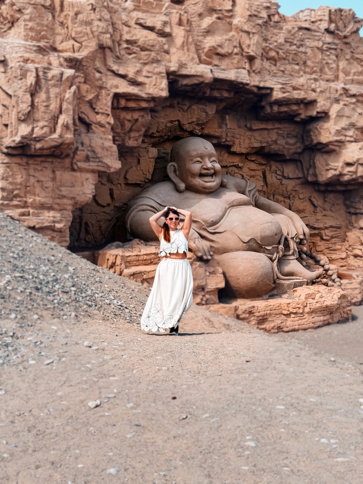 Linda posing in front of a giant Laughing Buddha carved into the cliff, Dunhuang Silk Road Heritage City