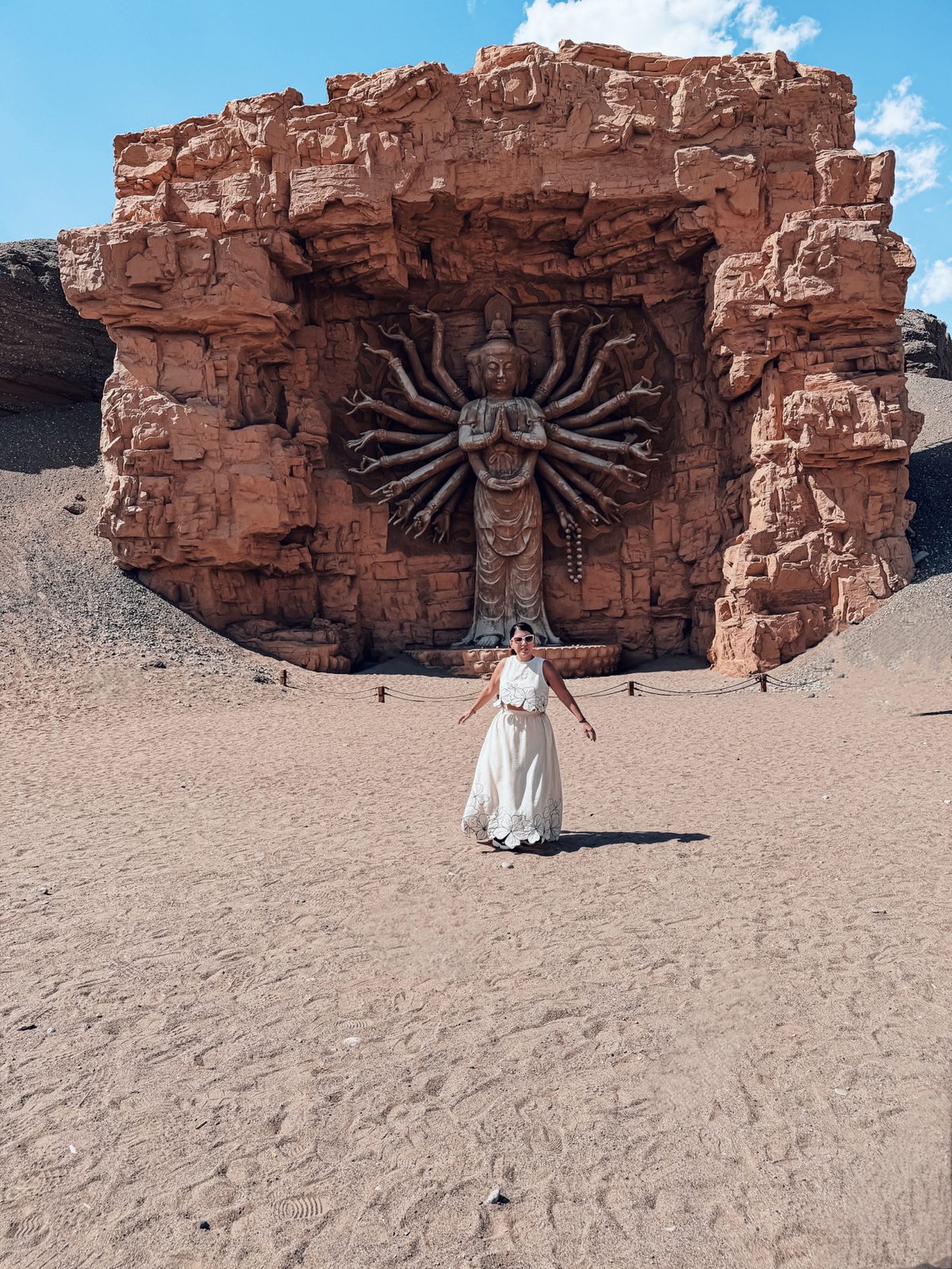Linda in front of the thousand armed Guanyin carved into a red cliff at the Dunhuang Silk Road Heritage City