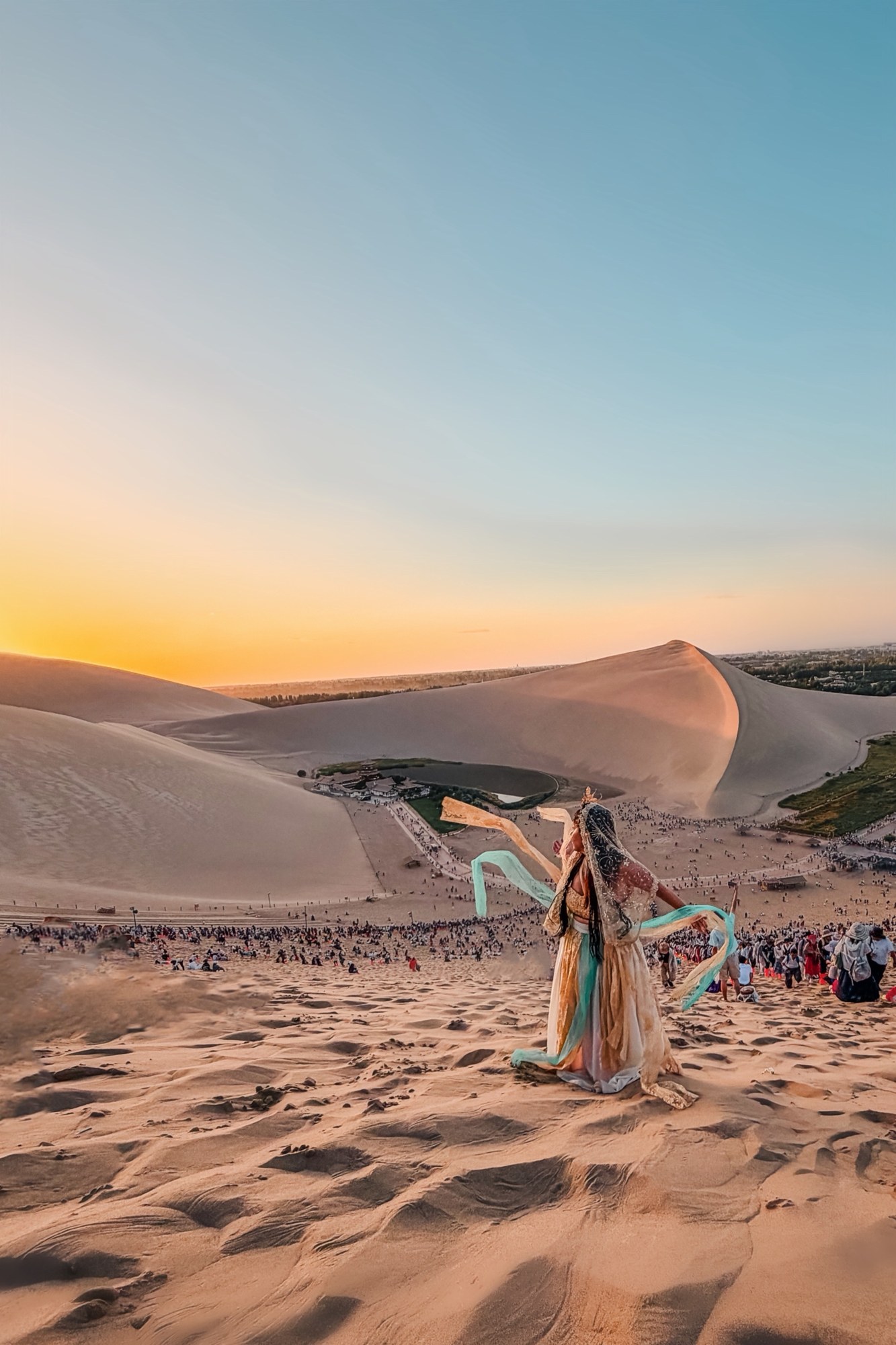 Linda in an apsara style costume with flowing ribbons on the Mingsha Shan dunes at sunset, Crescent Lake below
